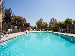 A serene outdoor hotel swimming pool with clear blue water, surrounded by a neat patio area with lounging chairs 